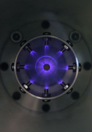 Head-on view into a circular ignition chamber showing purple plasma discharges arcing radially inward from bolt electrodes toward a central point.