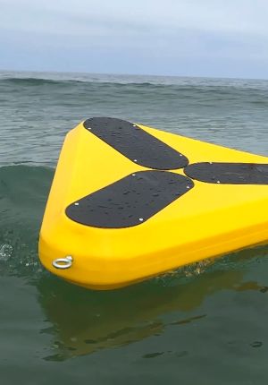 Close-up of a triangular yellow floating platform with black solar panels partly awash in grey-green ocean swell.