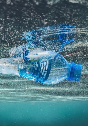 Close-up underwater shot of a crumpled blue plastic water bottle floating just below the surface, surrounded by rising air bubbles.