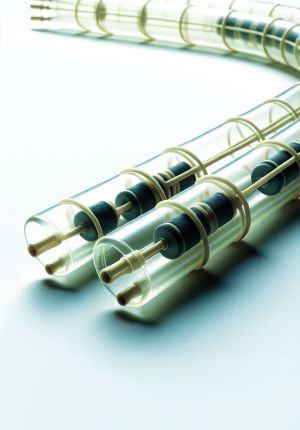 Close-up of transparent tubular hydrophone or sensor assemblies with dark internal elements and ribbed housings, arranged on a pale surface.